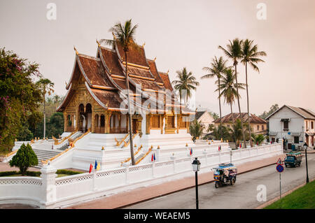 APR 4, 2019 Luang Prabang, Laos - Luang Prabang Royal Palace Museum und Hor Prabang Temple Hall unter der Kokospalme mit Tuk Tuk auf Morgen ruhig stree Stockfoto