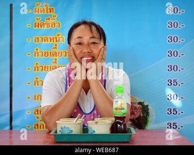 Thai Frauen kochen und Co - Inhaber von einem lokalen Restaurant posiert vor der Menü-/Preisliste und Lächeln für die Kamera. Stockfoto