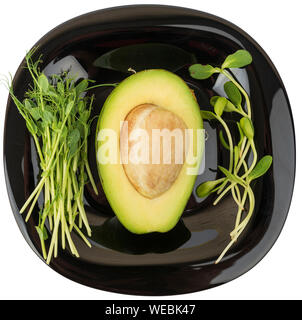 Veganes Frühstück. Avocado- und Micro grünen Sprossen auf einer schwarzen Platte isoliert auf Weiss. Stockfoto