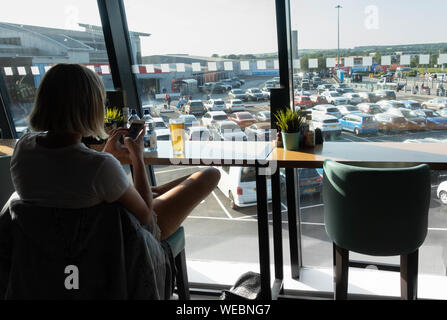 Junge Frau mit einem Glas Bier/Lager im Airport Departure Lounge Bar. Großbritannien Stockfoto