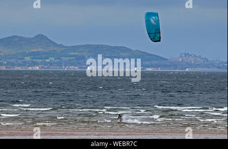 Longniddry Bents, East Lothian, Schottland, Großbritannien. 30 Aug, 2019. Eine einsame Kite Surfer aus Kiteboarding trotzt der abgehackt Firth-of-Forth und böigem Wind am Longniddry wo Stumpf trostlosen Bedingungen zu einer Aufhellung Himmel am Mittag gab, mit Edinburgh Castle und Arthur's Seat im Hintergrund. Geschätzte Wind: 42km/h SW. Böen: 63 km/h. Stockfoto