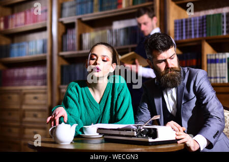 Das studentische Leben in der Universität. Paar in der Bibliothek mit Schreibmaschine und Kännchen Kaffee Trinken aus dem Becher. Literatur Cafe mit bärtigen Mann und nettes Mädchen. agil Stockfoto