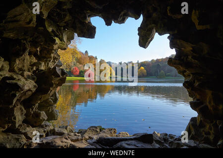 Blick von der Grotte über den See zu den entfernten Brücke und farbenfrohe Bäume an Stourhead Wiltshire UK im späten Herbst Stockfoto