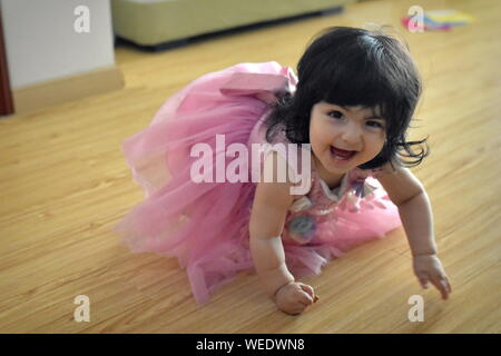 Cute Baby Mädchen kriecht in Pink Princess Dress und grinsend Stockfoto