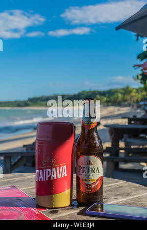 BAHIA, BRASILIEN - 27. Juni 2019: Der Blick auf eine kalte Flasche Bier mit Wassertropfen, in der Nähe von einem Menü und ein Smartphone in einem hölzernen Tisch von einem Kiosk durch die Stockfoto