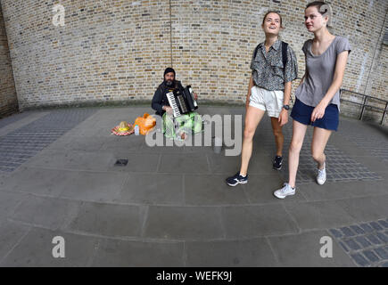 London, England, UK. Zwei Mädchen zu Fuß hinter einem Gaukler spielen auf dem Akkordeon, in Southwark Stockfoto