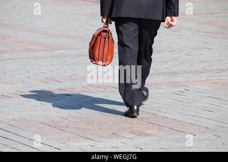 Mann in einen Anzug tragen leder Aktentasche zu Fuß auf einer Straße, schwarze Schatten auf Pflaster. Konzept der Geschäftsmann, Beamter, Politiker, Karriere Stockfoto