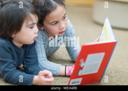 Junge Mädchen lesen Buch, jüngeren Bruder im Hintergrund spielen Stockfoto