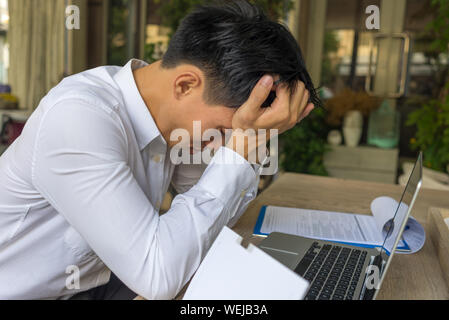 Frustriert Geschäftsmann holding Kopf während der Arbeit, die auf Notebook- und Papierarbeiten Stockfoto