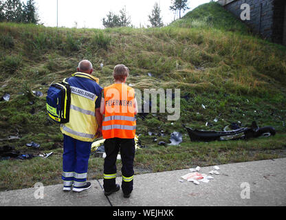 Bad Lobenstein, Deutschland. 30 Aug, 2019. Ein Pfarrer und ein Mitglied der Feuerwehr sind stehend an einer Unfallstelle auf der Autobahn 9 vor einem Bahndamm mit Schmutz bedeckt ist. Am Nachmittag, ein kleiner Lkw fuhr zwischen Bad Lobenstein und Schleiz in eine Gruppe von drei Motorräder von vier Menschen, die wahrscheinlich Schutz vor dem Regen unter einer Brücke gesucht hatten, belegt. Die motorradfahrer starb noch an der Unfallstelle. (Zu dpa: "Vier tote Motorradfahrer in einen schweren Unfall auf der A 9') Credit: Bodo Schackow/dpa-Zentralbild/dpa/Alamy leben Nachrichten Stockfoto