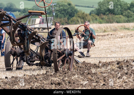 Haselbury Plucknet. Somerset. Vereinigtes Königreich. 18. August 2019. Ein Pflug wird über ein Feld von einer voll restaurierten alten Zugmaschine gezogen zu einem Stockfoto