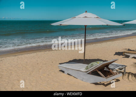 Eine entspannende Atmosphäre in der Nähe des Meeres mit einer stützenden bequemen Sessel und einem weißen Sonnenschirm in einem Resort Hotel an einem paradiesischen tropischen Strand ideal für Su Stockfoto