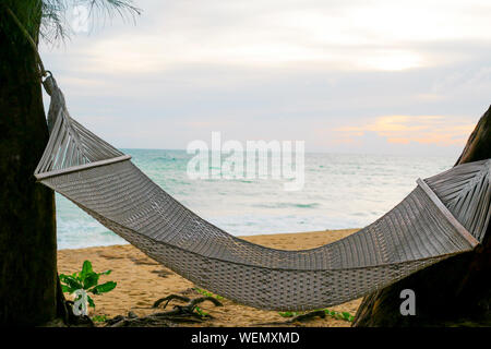 Weiße Seil Krippe hängt zwischen den Bäumen in der Nähe der Strand und das Meer im Sonnenuntergang, die entspannend und frische Lifestyle Stockfoto