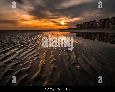 Sonnenuntergang mit Sun spähen durch die bedeckt am Strand mit Sand Wellen im Vordergrund bei Ebbe Stockfoto