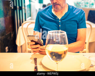 Mann mit blauem Hemd in der Tabelle der ein Restaurant mit seinem Handy Stockfoto