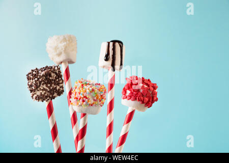 Süße chewy Eibisch und Lutscher auf Stroh dekoriert mit geschmolzener Schokolade und Kuchen auf blauem Hintergrund Streuseln. Kinder lieben diese. Cop Stockfoto