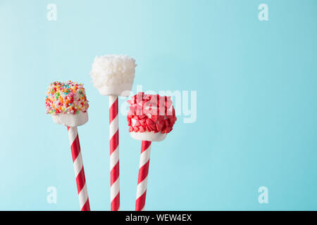 Süße chewy Eibisch und Lutscher auf Stroh dekoriert mit geschmolzener Schokolade und Kuchen auf blauem Hintergrund Streuseln. Kinder lieben diese. Cop Stockfoto