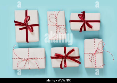 Mehrere Weihnachtsgeschenke verpacken in dekorativen Papier mit roter Schleife Laing auf blauem Hintergrund. Flach. Ansicht von oben. Stockfoto