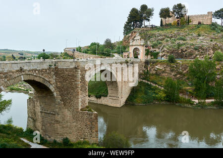 TOLEDO, Spanien - 24 April 2018: Ausblick auf die barocke Triumphbogen auf der Alcantara Brücke über den Fluss Tejo und die Burg in San Servando Toledo. Stockfoto