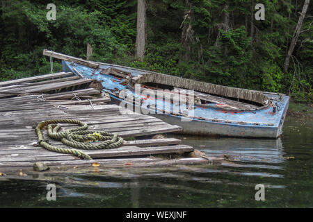 Ein verfallenes, stripped down Alte dayboat in den Untiefen zu einem baufälligen Dock sitzt auf einem bewaldeten Ufer in einer ruhigen Gegend an der Küste von Britisch-Kolumbien. Stockfoto