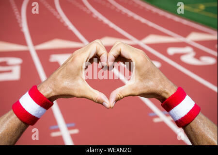 Japanischen Athleten mit roten und weißen farbige Armbänder, liebe Herzen Hände Geste gegen eine rote Leichtathletikbahn Hintergrund Stockfoto