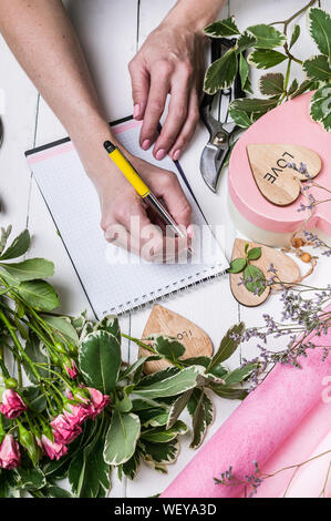 Blumengeschäft arbeitet. Frauen Hände schreiben Sie eine Bestellung einen Strauß Rosen und viel Grün. Small Business Konzept. Vertikaler Dampfstoß Stockfoto