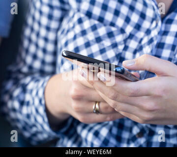 Junge Frau in blau kariertem Hemd gekleidet, mit modernen Smartphone, weibliche Hände schreiben Sms über Handy, Social Networking anhand von quantitativen Simulatio Stockfoto