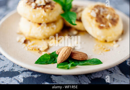 Käsekuchen, Quark Pfannkuchen mit Mandeln, frische Minze und Ahornsirup auf einem grauen Hintergrund von einer konkreten Tabelle. Käsekuchen, hausgemachte tradit Stockfoto