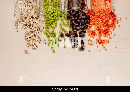 Eine Reihe von verschiedenen getrockneten Hülsenfrüchten ist in Glas Tassen und ist ein wenig zerstreut: Rote Linsen, Erbsen, rote Bohnen, weiße Bohnen. Hülsenfrüchte am oberen Rand. Stockfoto