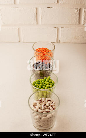 Sammlung von verschiedenen getrockneten Hülsenfrüchten in Glas Gläser vertikal grüne Erbsen, rote Linsen, rote Bohnen, weiße Bohnen close-up auf einem weißen Hinterg Stockfoto