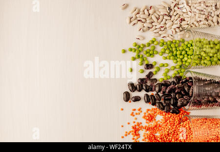 Eine Reihe von verschiedenen getrockneten Hülsenfrüchten ist in Glas Tassen und ist ein wenig zerstreut: Rote Linsen, Erbsen, rote Bohnen, weiße Bohnen. Hülsenfrüchte auf der rechten Sid Stockfoto