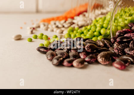 Eine Reihe von verschiedenen getrockneten Hülsenfrüchten ist in Glas Tassen und ist ein wenig zerstreut: Rote Linsen, Erbsen, rote Bohnen, weiße Bohnen. Selektiver Fokus auf Rot B Stockfoto