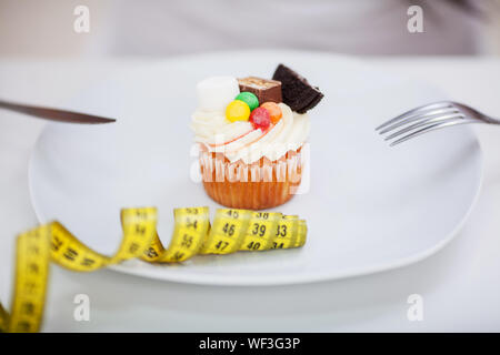 Junge nährende Frau sitzen vor der Platte mit lecker Sahne Torte Kuchen, bei verboten, Lebensmittel mit unglücklich und hungrigen Ausdruck suchen, Studio Stockfoto