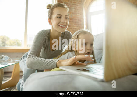 Weiblichen kaukasischen Lehrer und kleine Mädchen, oder Mutter und Tochter. Homeschooling. Auf dem Sofa sitzen und mit Laptop für Kenntnisse erhalten während der Lektion ist. Bildung, Schule, Studium Konzept. Stockfoto