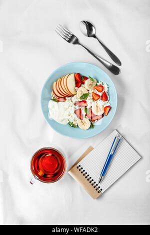 Gesunde blaue Platte mit Obst Salat mit Erdbeeren und Quark, Tasse starken Kaffee, Notebook mit leeren Seite und blauen Stift auf weißem Tabelle. Con Stockfoto