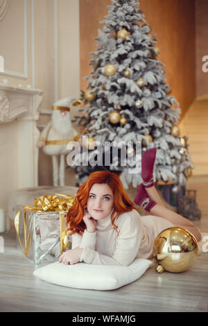 Glückliche junge Dame mit curlu Haar Geschenke durch den Kamin in der Nähe der Weihnachtsbaum. Neues Jahr Konzept. Stockfoto