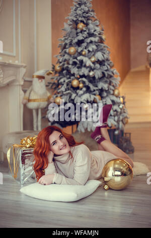 Glückliche junge Dame mit curlu Haar Geschenke durch den Kamin in der Nähe der Weihnachtsbaum. Neues Jahr Konzept. Stockfoto