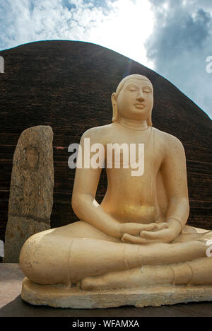 Ein sitzender Buddha Statue sitzt vor einem Abschnitt des roten Backstein Sandagiri Stupa in Tissamaharama in Sri Lanka. Stockfoto