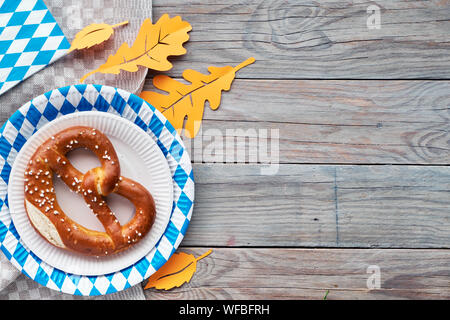 Oktoberfest im Hintergrund. Pezel in blau und weiß karierten Einweg Pappteller. Flach auf rustikalen Holztisch mit Blätter im Herbst eingerichtet Stockfoto