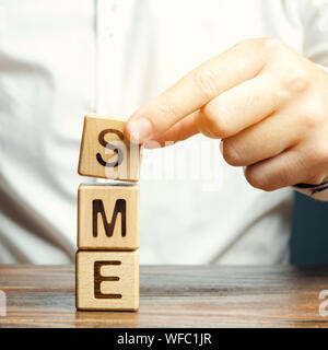 Unternehmer hält Holzblöcke mit dem Wort KMU. Kleine und mittlere Unternehmen, gewerbliche Unternehmen, die nicht bestimmte Indikatoren nicht überschreiten. Stockfoto