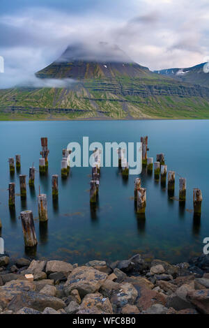 Reydarfjordur Hafen mit glatten Wasser und Beiträge im Wasser an einem sonnigen Sommertag im Osten von Island Stockfoto