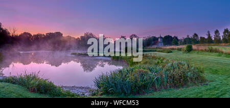 Stoke Charity, Großbritannien - 21.August 2019: Dawn Licht und Nebel auf der alten Mühle Teich im Dorf Stoke Charity mit der Kirche von St. Michael in der Dis Stockfoto