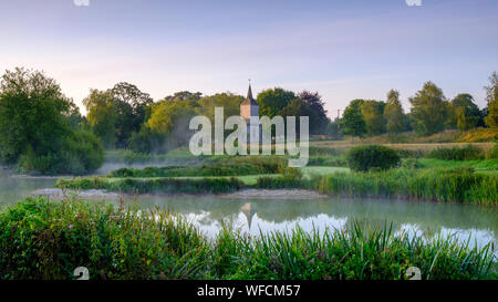 Stoke Charity, Großbritannien - 21.August 2019: Dawn Licht und Nebel auf der alten Mühle Teich im Dorf Stoke Charity mit der Kirche von St. Michael in der Dis Stockfoto