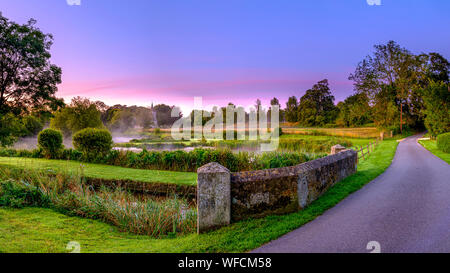 Stoke Charity, Großbritannien - 21.August 2019: Dawn Licht und Nebel auf der alten Mühle Teich im Dorf Stoke Charity mit der Kirche von St. Michael in der Dis Stockfoto