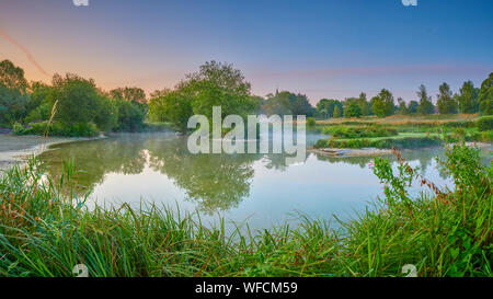 Stoke Charity, Großbritannien - 21.August 2019: Dawn Licht und Nebel auf der alten Mühle Teich im Dorf Stoke Charity mit der Kirche von St. Michael in der Dis Stockfoto