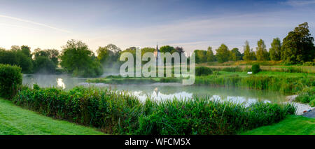 Stoke Charity, Großbritannien - 21.August 2019: Dawn Licht und Nebel auf der alten Mühle Teich im Dorf Stoke Charity mit der Kirche von St. Michael in der Dis Stockfoto