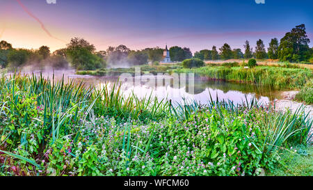 Stoke Charity, Großbritannien - 21.August 2019: Dawn Licht und Nebel auf der alten Mühle Teich im Dorf Stoke Charity mit der Kirche von St. Michael in der Dis Stockfoto