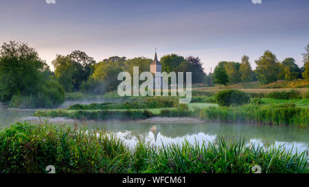 Stoke Charity, Großbritannien - 21.August 2019: Dawn Licht und Nebel auf der alten Mühle Teich im Dorf Stoke Charity mit der Kirche von St. Michael in der Dis Stockfoto