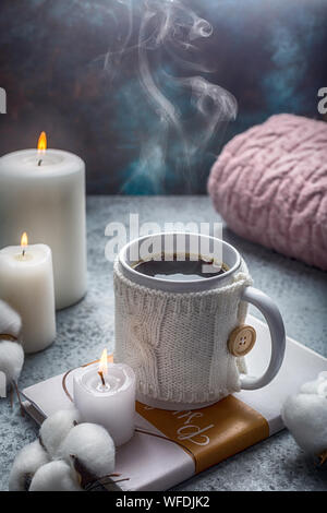 Tasse heißen Getränk in Weiß gestrickte Decken auf dem Buch Kerzen und Baumwolle um hugge Stil Stockfoto