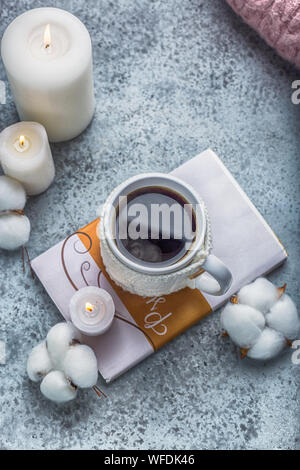 Tasse heißen Getränk in Weiß gestrickte Decken auf dem Buch Kerzen und Baumwolle um hugge Stil Stockfoto